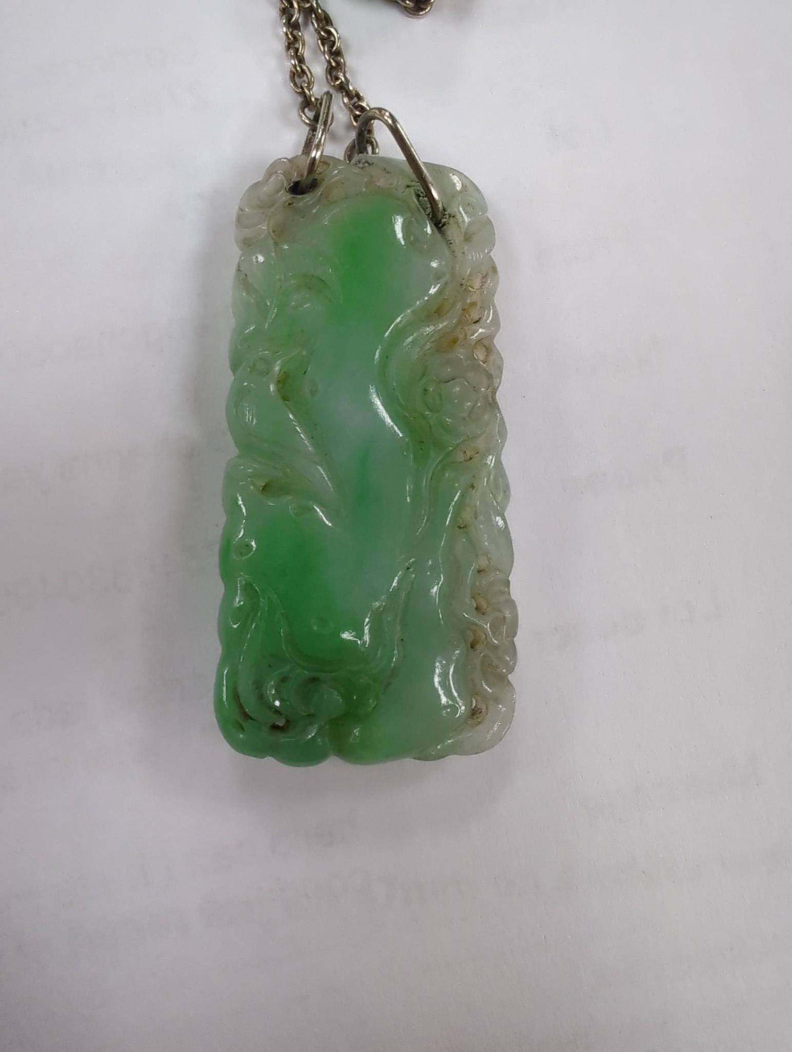 Two carved jade pendants, largest 47mm on a white metal chain.